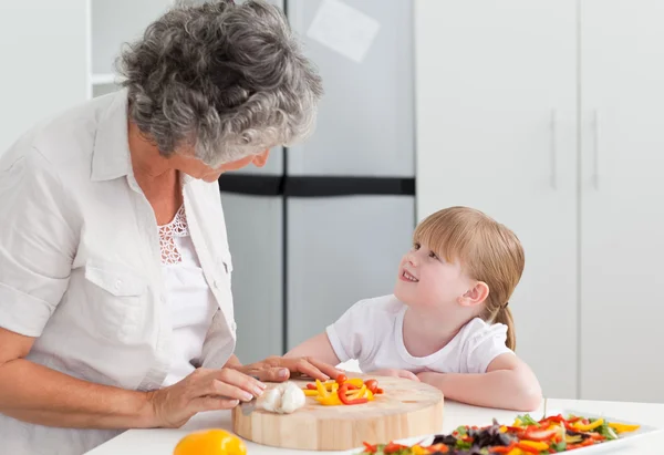Маленькая девочка смотрит на свою бабушку, которая готовит — стоковое фото