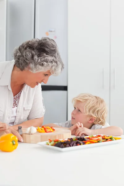 Little boy looking at his grandmother cooking at home — Stock Photo, Image