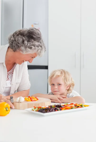 Маленький мальчик смотрит, как его бабушка готовит дома — стоковое фото