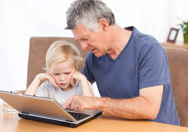 Śliczny chłopiec i jego dziadek, patrząc na laptopa — Zdjęcie stockowe