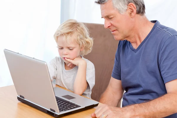 Lindo menino e seu avô olhando para seu laptop — Fotografia de Stock