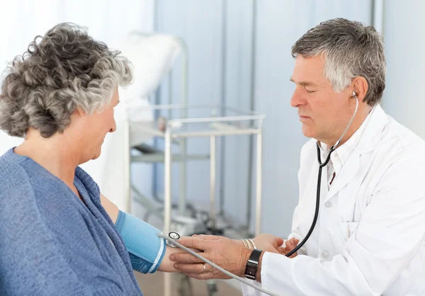 Un médico mayor tomando la presión arterial de su paciente —  Fotos de Stock