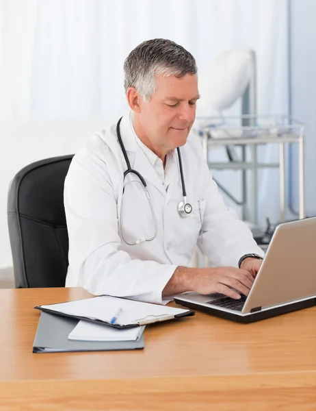 Een senior arts werkzaam op zijn laptop in zijn kantoor — Stockfoto