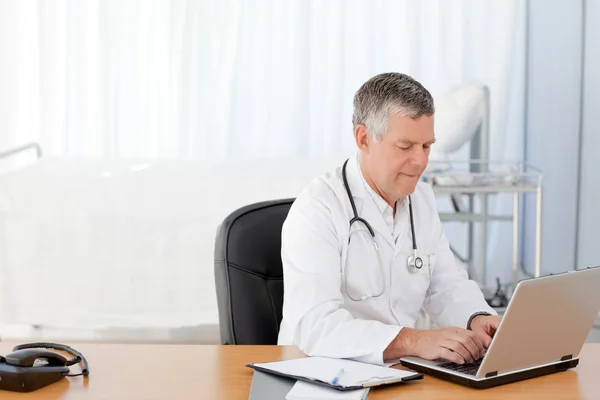 Starszy lekarz pracuje na swoim laptopie w jego biurze — Zdjęcie stockowe
