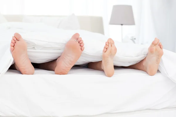 Koppel de voeten in het bed — Stockfoto