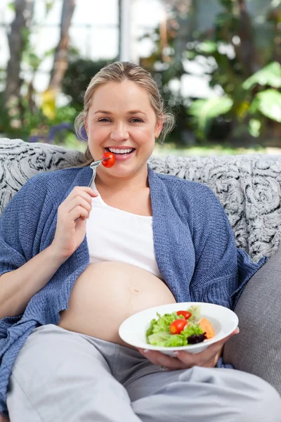 Беременная женщина ест овощи на диване — стоковое фото