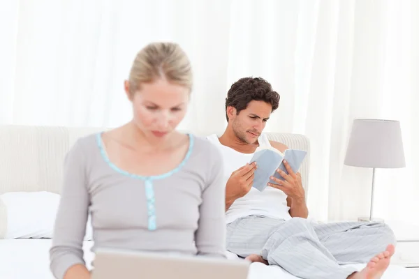 Femme travaillant sur son ordinateur portable pendant que son mari lit — Photo
