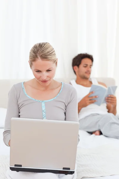 Женщина работает над своим ноутбуком, пока ее муж читает — стоковое фото