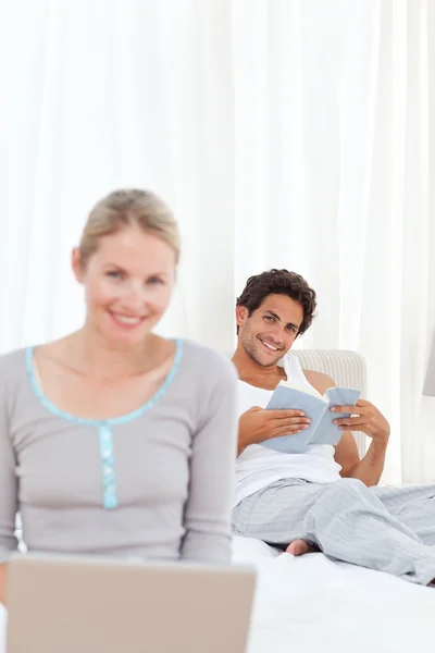 Woman working on her laptop while her husband is reading — Stock Photo, Image