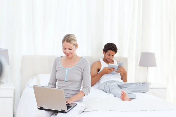 Femme travaillant sur son ordinateur portable pendant que son mari lit — Photo