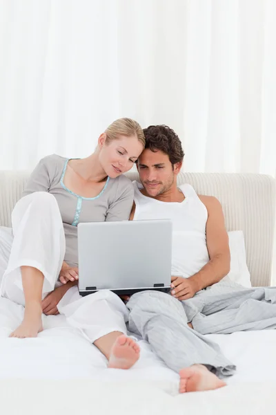 Очаровательная пара смотрит на свой ноутбук на кровати — стоковое фото
