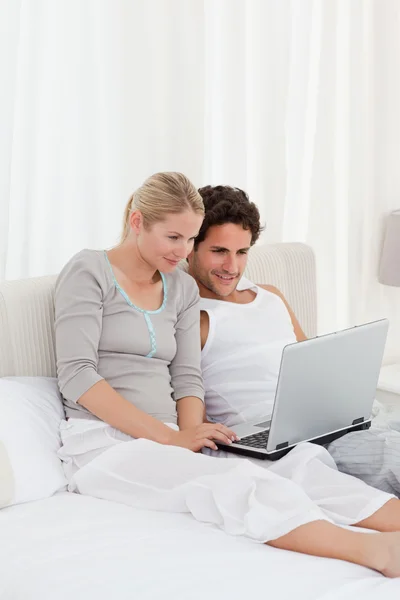 Очаровательная пара смотрит на свой ноутбук на кровати — стоковое фото