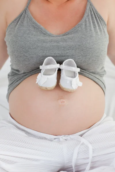 Радостная беременная женщина в детской обуви на животе — стоковое фото