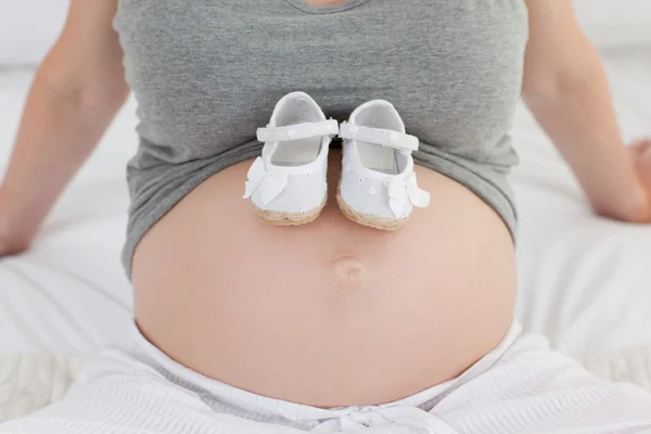 彼女の腹の子供の靴とうれしそうな妊娠中の女性 — ストック写真