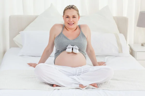 Vrolijke zwangere vrouw met childrens schoenen op haar buik — Stockfoto
