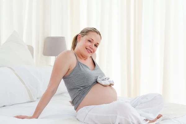 Радостная беременная женщина в детской обуви на животе — стоковое фото