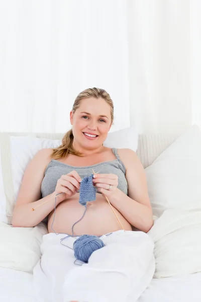 Entzückende schwangere Frau strickt auf ihrem Bett — Stockfoto