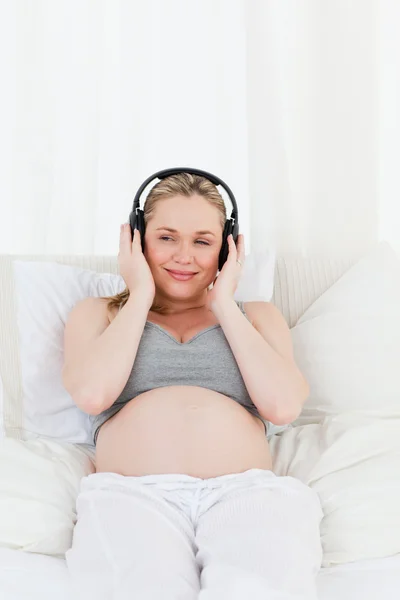 Bella donna incinta che ascolta musica sul suo letto — Foto Stock