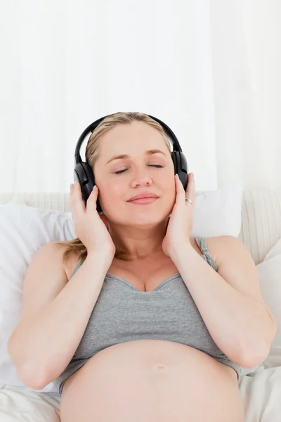 Mujer embarazada encantadora escuchando música en su cama — Foto de Stock