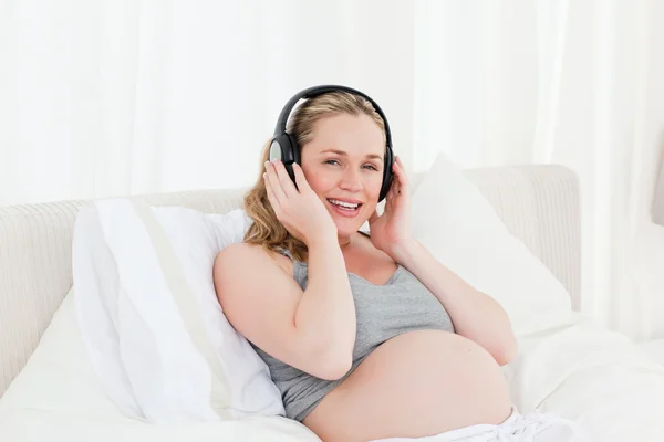 Belle femme enceinte écoutant de la musique sur son lit — Photo