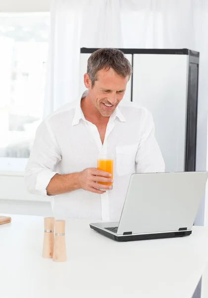 Man looking at his laptop while he is drinking oranje juice — Stock Photo, Image