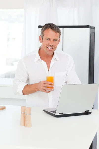 Man looking at his laptop while he is drinking oranje juice — Stock Photo, Image