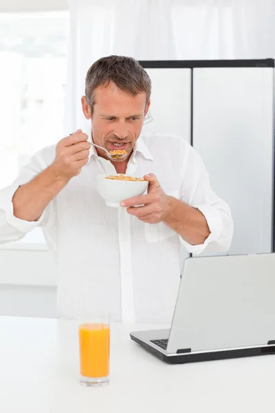 Man eten granen terwijl hij aan zijn laptop werkt — Stockfoto