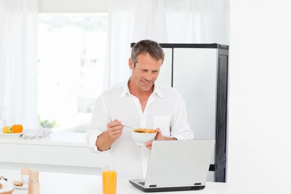 Mann isst Müsli, während er an seinem Laptop arbeitet — Stockfoto