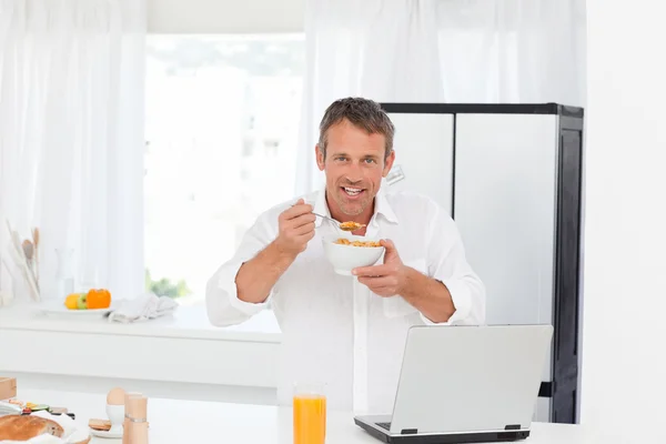 Mężczyzna jedzenie zbóż a pracuje na swoim laptopie — Zdjęcie stockowe