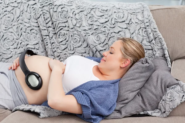 Jeune femme mettant ses écouteurs sur son ventre — Photo