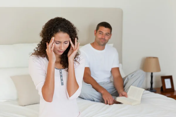 Vrouw met een hoofdpijn, terwijl haar echtgenoot is lezen — Stockfoto