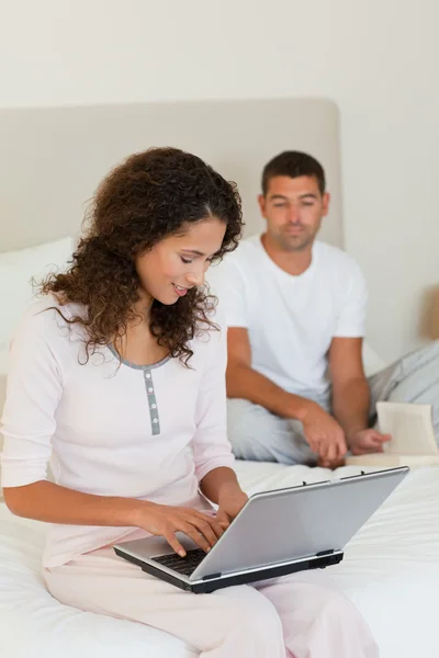 Žena pracující na svém laptopu, zatímco její manžel je čtení — Stock fotografie