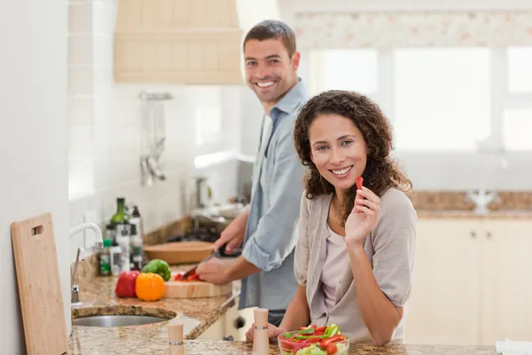 Woman eating while her husband is cooking — Stock Photo, Image