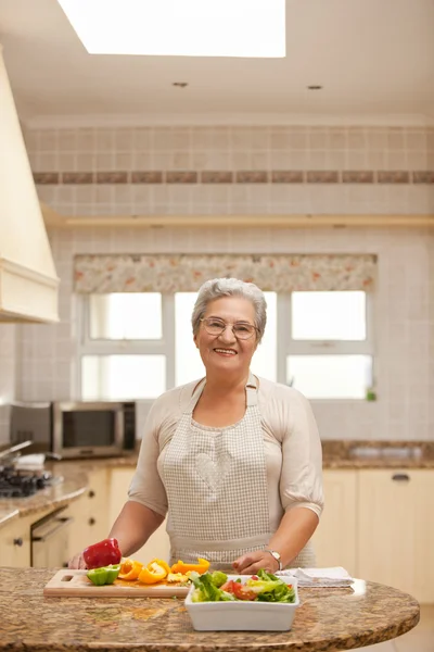 退休的女人看着在厨房里的相机 — 图库照片