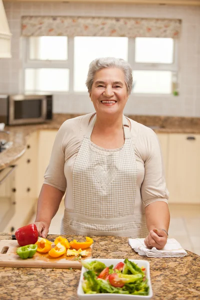 Pensionerad kvinna som tittar på kameran i köket — Stockfoto