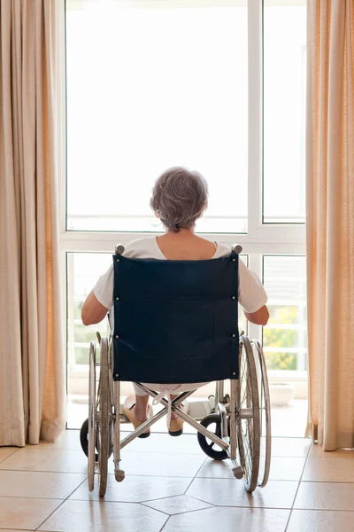 Mogen kvinna i hennes rullstol med henne tillbaka till kameran — Stockfoto