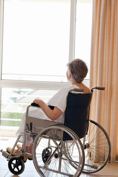 Starszy kobieta w jej wózek inwalidzki, patrząc przez okno — Zdjęcie stockowe