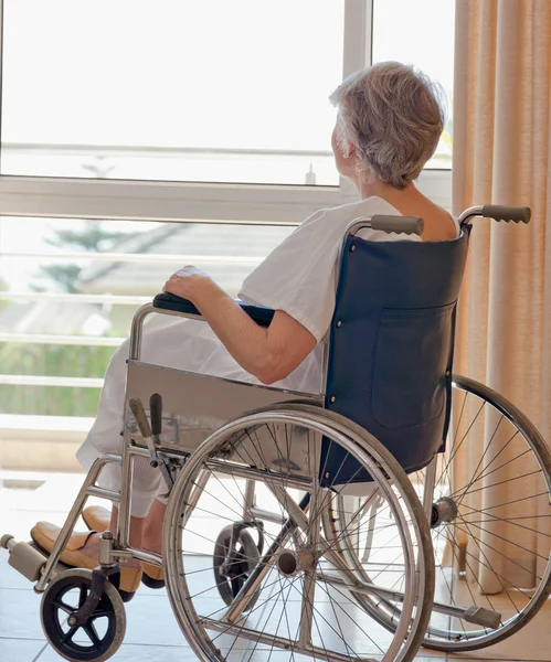 Senior vrouw in haar rolstoel kijkt uit het raam — Stockfoto