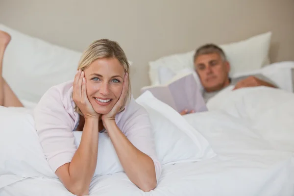 Hübsche Frau schaut in die Kamera, während ihr Mann schläft — Stockfoto