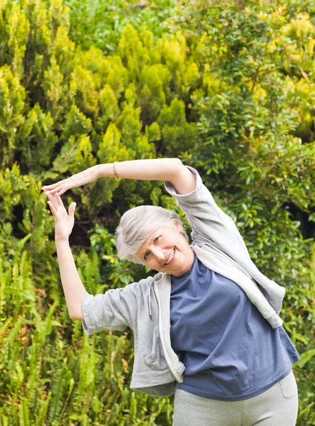 Mogen kvinna gör hennes sträcker i trädgården — Stockfoto