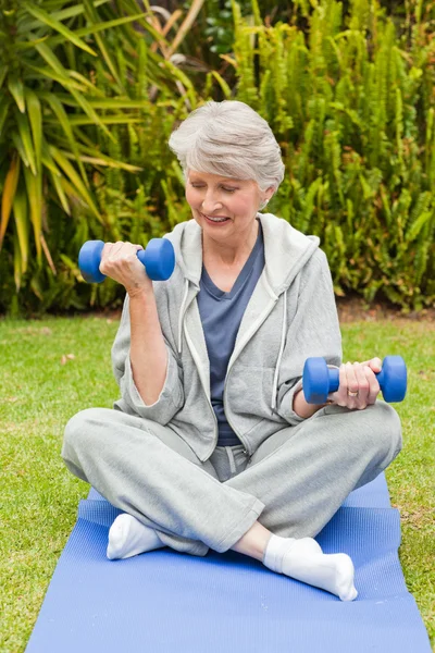 Pensionerad kvinna gör hennes övningar i trädgården — Stockfoto