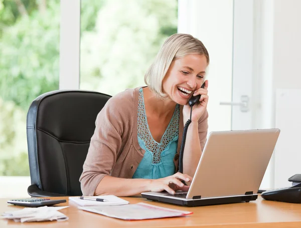 Kvinna som arbetar på hennes dator medan hon ringa — Stockfoto