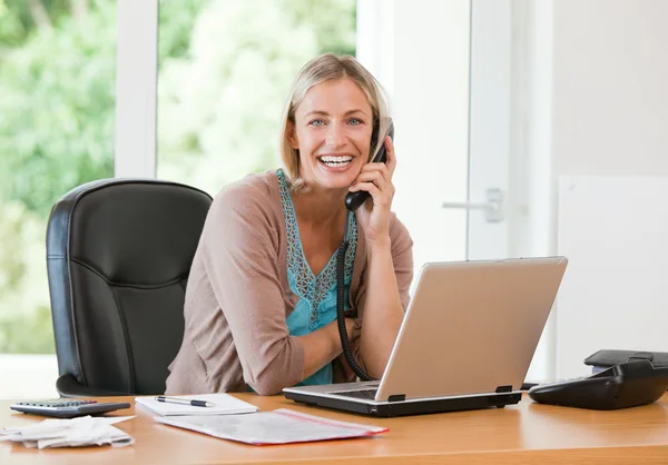 Vrouw die werkt op haar computer terwijl ze is bellen — Stockfoto