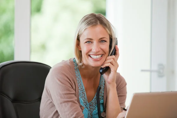 Vrouw die werkt op haar computer terwijl ze is bellen — Stockfoto