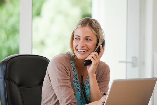 Frau arbeitet am Computer, während sie telefoniert — Stockfoto