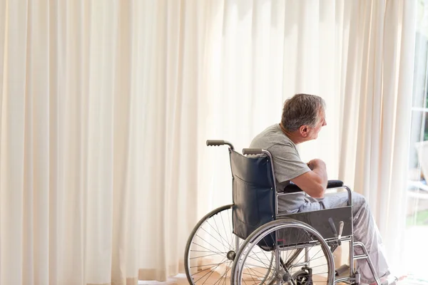 Человек в инвалидном кресле смотрит в окно — стоковое фото