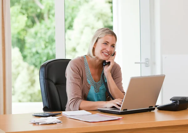Mulher trabalhando em seu computador enquanto ela está telefonando — Fotografia de Stock