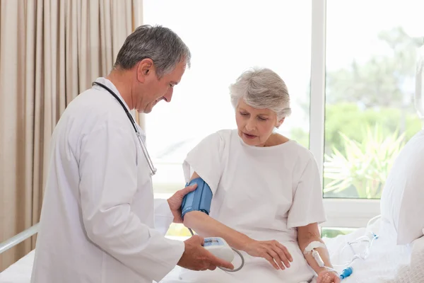 Mature doctor taking the blood pressure of his patient — Stock Photo, Image