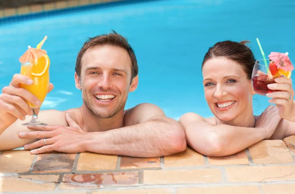 Beautiful couple drinking cocktails in the swimming pool — Stock Photo, Image