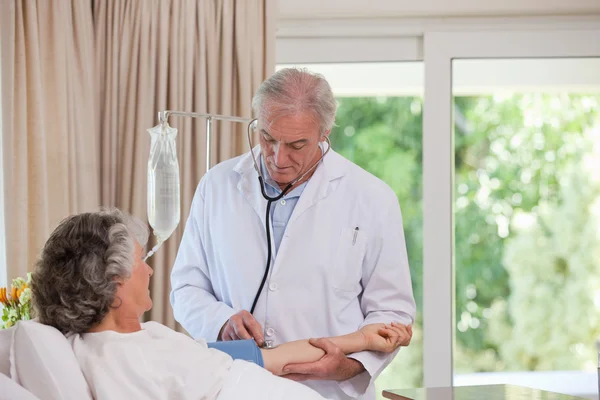 Senior arts nemen de bloeddruk van zijn patiënt — Stockfoto